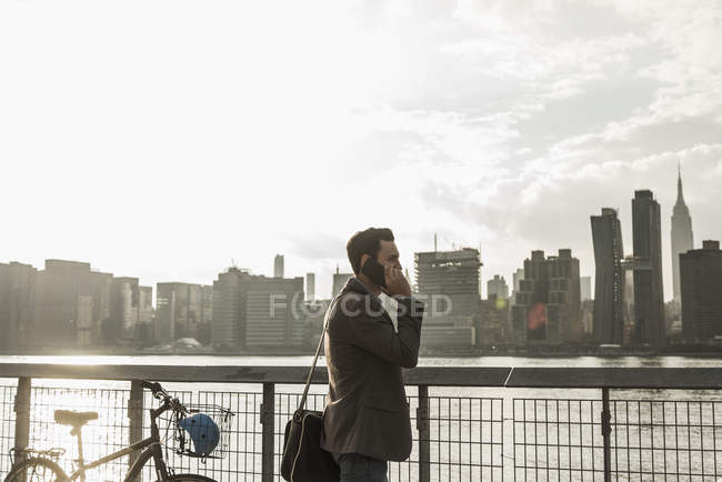 Hombre de negocios en el teléfono celular en East River, Nueva York, EE.UU. - foto de stock