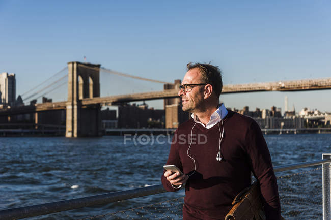 Соединенные Штаты Америки, Бруклин, бизнесмен со смартфоном, идущий перед Бруклинским мостом — стоковое фото