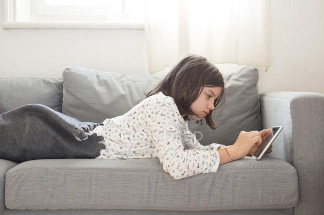 Chica acostada en el sofá y el uso de mini tableta - foto de stock