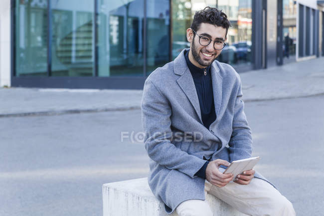 Портрет посміхаючись молодий чоловік з міні планшет, сидячи на тумб — стокове фото
