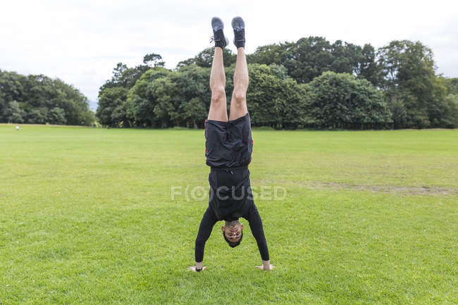 Handsome caucasian sporty man standing on hands in park — Stock Photo