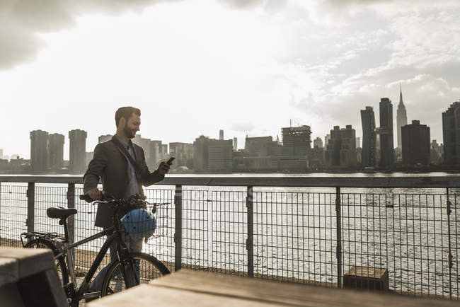 Geschäftsmann mit Fahrrad zu Fuß entlang des East River und mit dem Handy, New York City, USA — Stockfoto