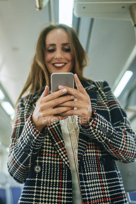 Smiling woman on a train looking at cell phone — Stock Photo