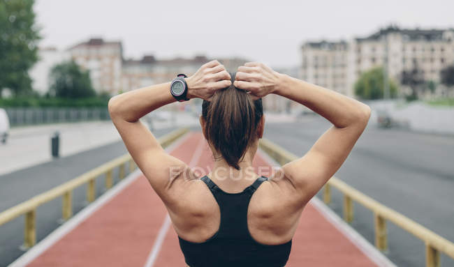 Vista trasera de la mujer en la pista de tartán atar su coleta - foto de stock