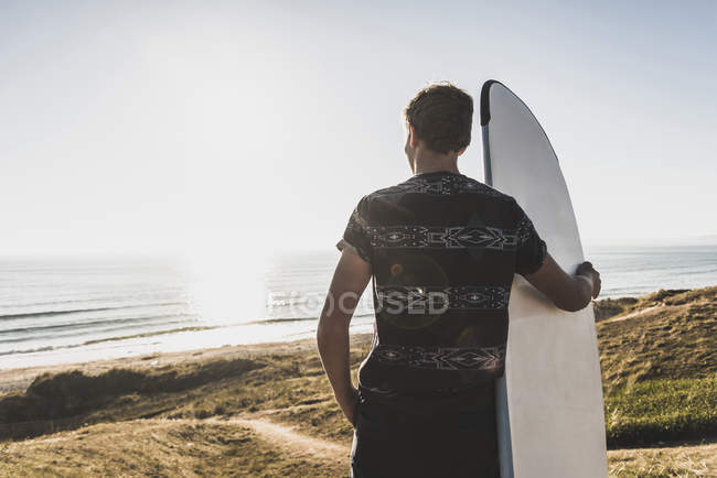 Vista posteriore del ragazzo adolescente con tavola da surf guardando verso il mare — Foto stock