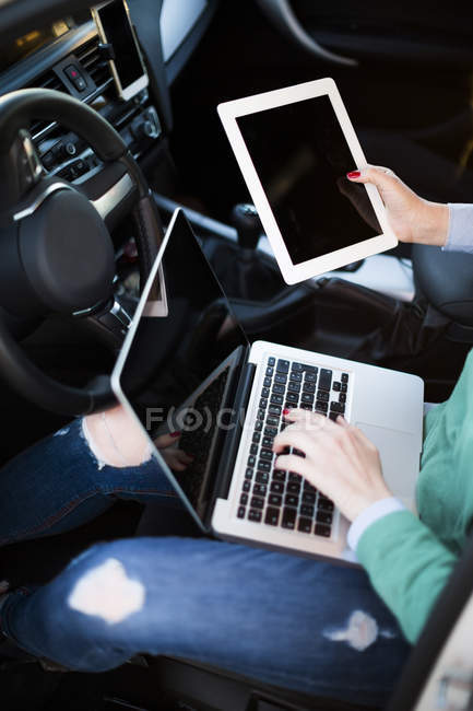 Mujer trabajando dentro de su coche con tableta digital y portátil - foto de stock