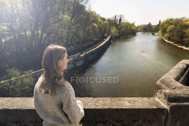 Giovane donna sul ponte guardando il fiume — Foto stock