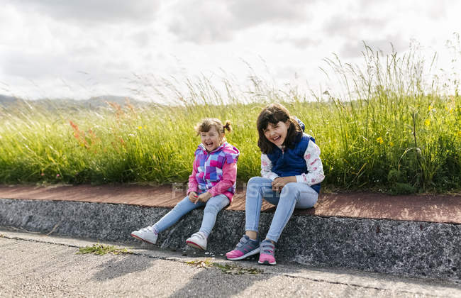Two laughing little sisters sitting at roadside — Stock Photo