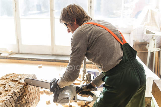 Sculpteur en bois en atelier travaillant le bois pour une sculpture avec une tronçonneuse — Photo de stock