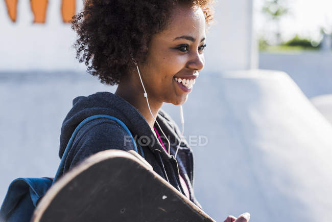 Smiling young woman with skateboard listening to music — Stock Photo