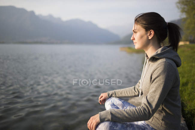 Itália, Lecco, jovem mulher relaxada sentada na margem do lago — Fotografia de Stock