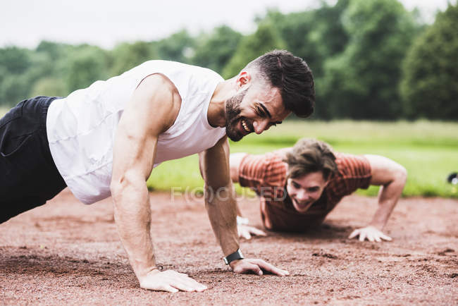 Two athletes doing pushups on sports field — Stock Photo