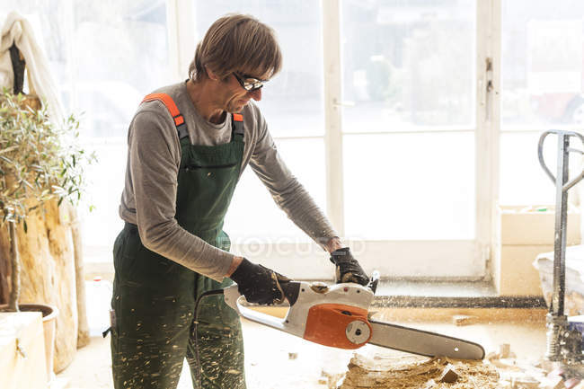 Sculpteur en bois en atelier travaillant le bois pour une sculpture avec une tronçonneuse — Photo de stock