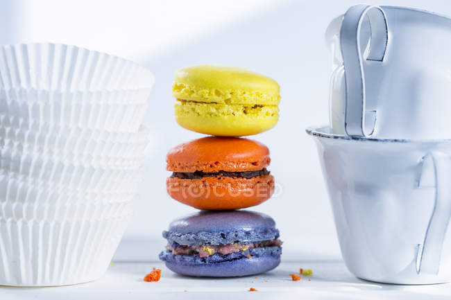 Stack of three colourful macarons, paper cups and two enamel cups — Stock Photo