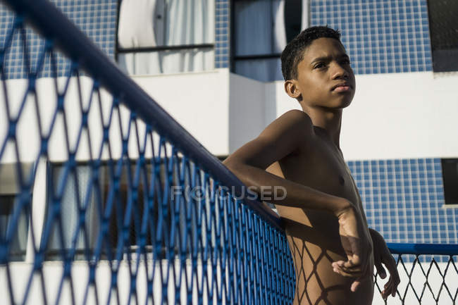 Teenager mit nacktem Oberkörper lehnt im Sonnenlicht an Zaun — Stockfoto