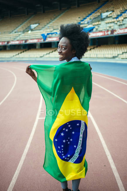 Joven atleta femenina en estadio portando bandera brasileña - foto de stock