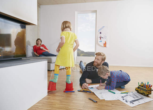 Father and son drawing on floor while mother and daughter having fun at