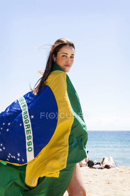 Молода брюнетка жінка грає з бразильським прапором на пляжі — стокове фото