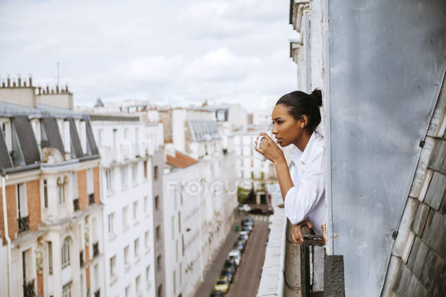 France, Paris, jeune femme avec une tasse de café penchée par la fenêtre — Photo de stock
