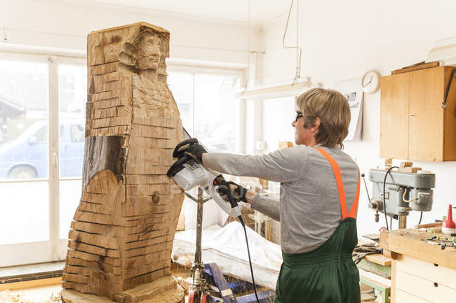 Wood carver in workshop working on sculpture with chainsaw — Stock Photo