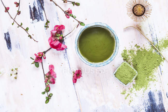 Chá Matcha em tigela com pó verde, colher, chasen e flores rosa — Fotografia de Stock