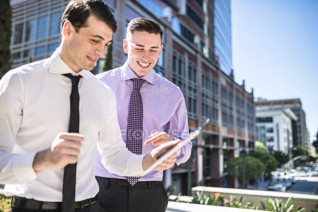 Два улыбающихся бизнесмена на улице смотрят на скрижаль — стоковое фото