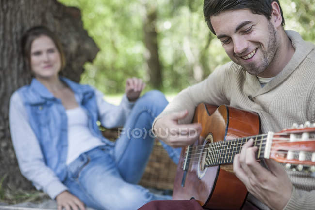 Jeune couple ayant un pique-nique avec homme jouant de la guitare — Photo de stock