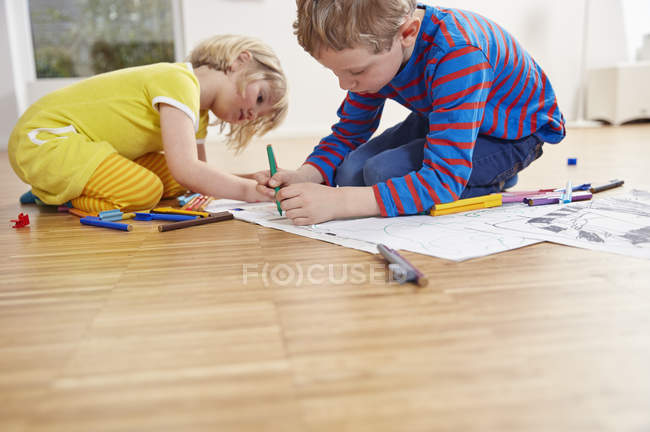 Brother and sister painting on wooden floor at home — Stock Photo