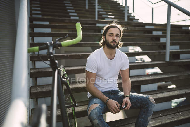 Young man sitting on stairs next to bike — Stock Photo