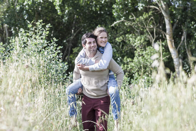 Young man carrying his girlfriend piggyback in the nature — Stock Photo