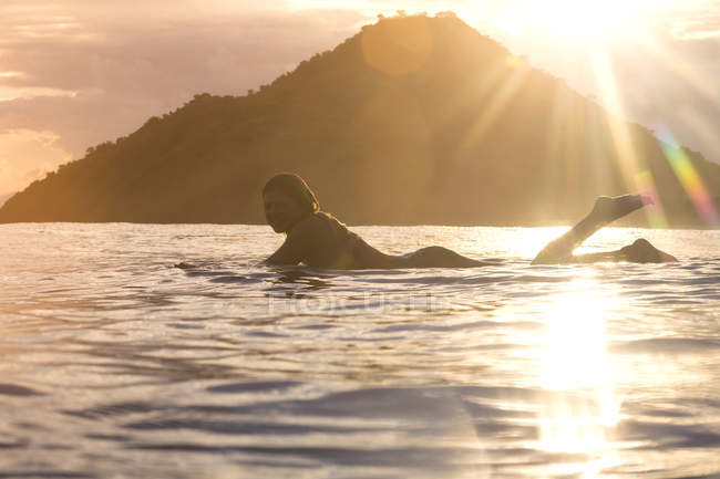 Indonesia, Sumbawa island, female surfer lying on surfboard in the evening — Stock Photo