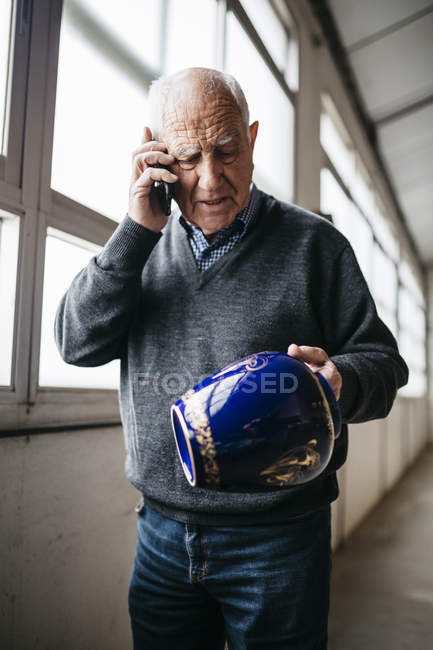 Elderly man reviewing the ceramic vase, talking on the phone — Stock Photo