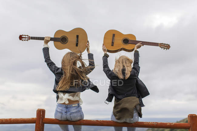 Deux femmes assises sur une clôture en bois soulevant des guitares — Photo de stock