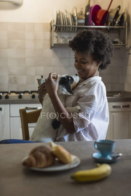 Femme assise à la table du petit déjeuner avec chien — Photo de stock