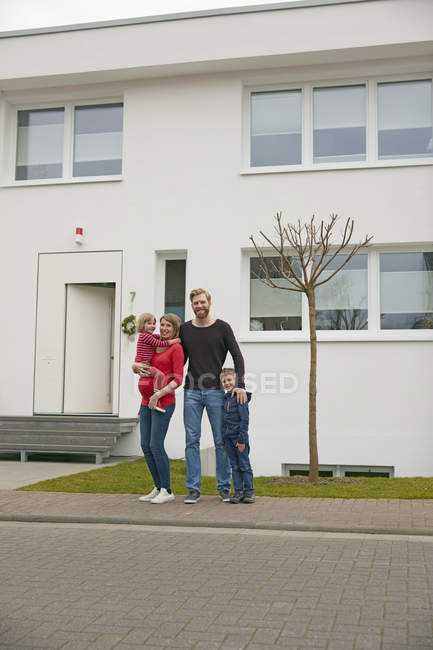 Retrato de familia feliz con madre embarazada delante de la casa - foto de stock