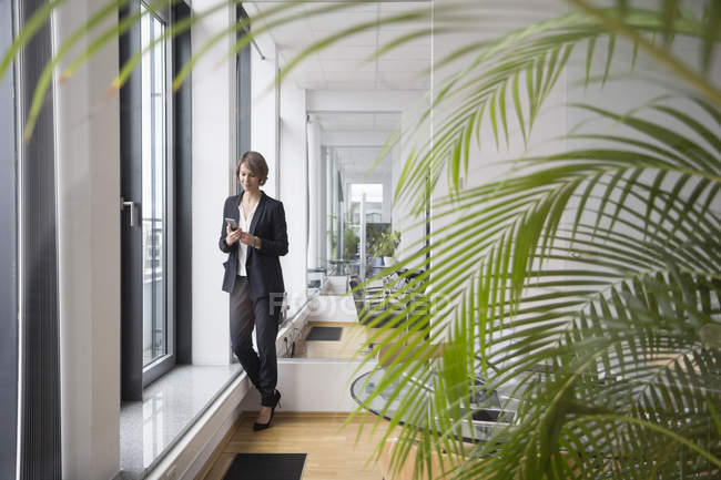 Geschäftsfrau benutzt Handy am Bürofenster — Stockfoto