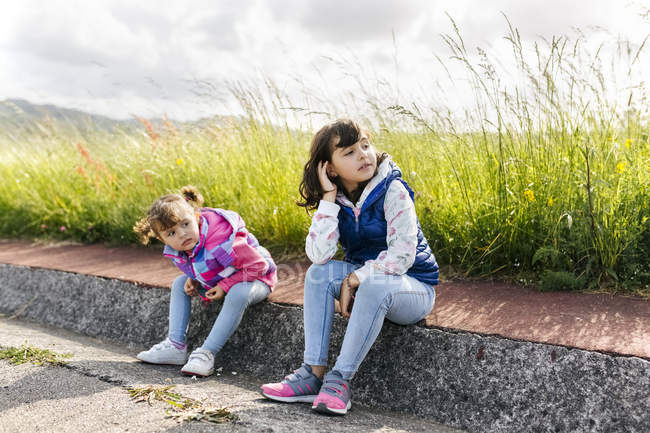 Two little sisters sitting on curb looking at distance — Stock Photo