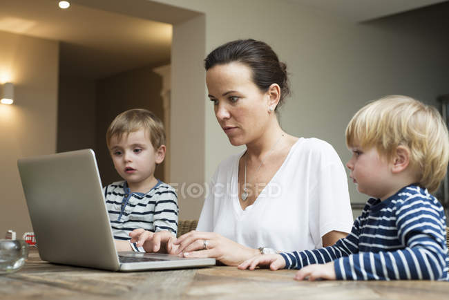 Madre usando laptop con sus hijos sentados a su lado - foto de stock