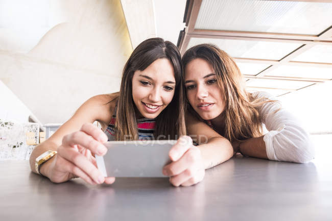Two female friends looking at cell phone — Front View, relaxed - Stock ...