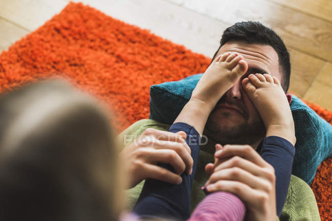 Игривая дочь, стоящая на лице отца на ковре на полу — стоковое фото