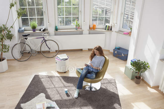 Жінка вдома, сидячи в кріслі, використовуючи цифровий планшетний — стокове фото