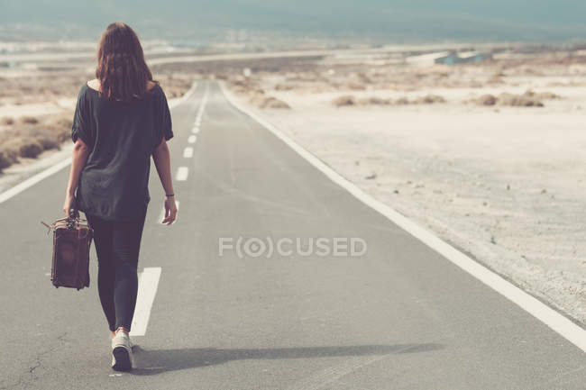 Mujer joven con maleta caminando por un camino - foto de stock