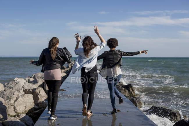 Three young women having fun on breakwater at the sea — Stock Photo
