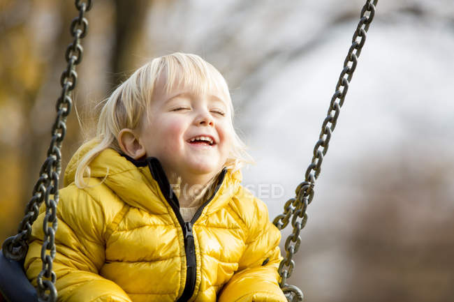 Niño vistiendo chaqueta amarilla con los ojos cerrados en swing - foto de stock