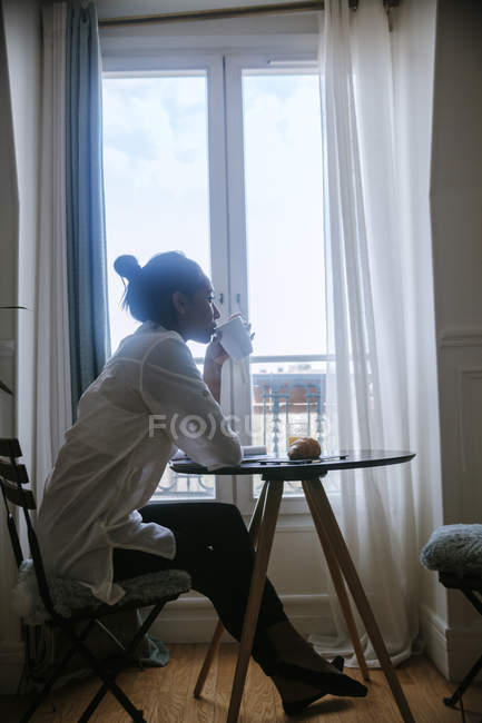 Jeune femme assise à la table du petit déjeuner buvant du café — Photo de stock