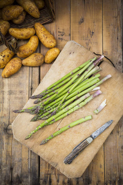 Asperges vertes et couteau sur planche à découper — Photo de stock