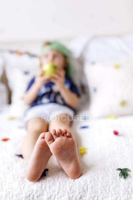 Piedi di bambino seduto sul divano a mangiare una mela — Foto stock