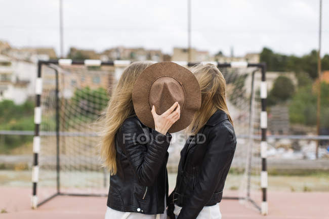 Dos mujeres de pie en el campo de deportes cubiertas con sombrero - foto de stock