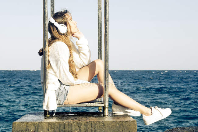 Adolescente escuchando música con auriculares cerca del mar - foto de stock