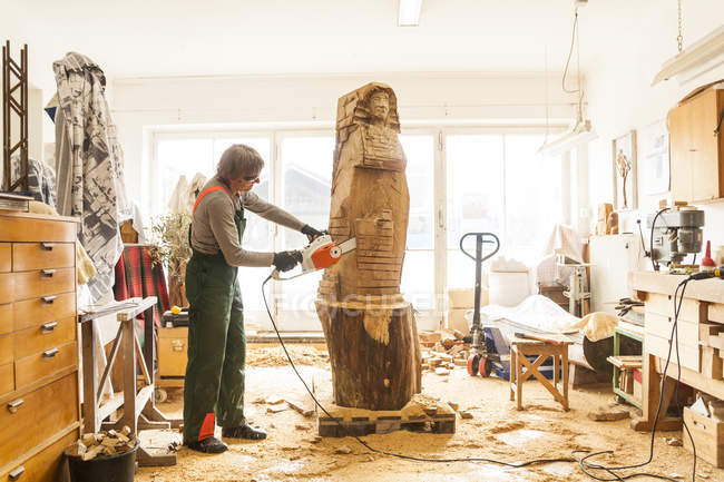 Sculpteur en bois en atelier travaillant sur la sculpture avec tronçonneuse — Photo de stock